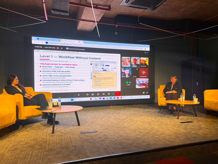 The hybrid panel in Tbilisi: two participants on stage and, on the screen behind them, the author presenting the slide “Level 1 — Workflow Without Content”.